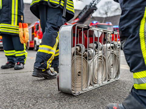 Eine Kiste mit mehreren Feuerwehrschläuchen steht zwischen mehreren Personen