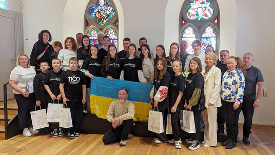 Das Foto zeigt die 30-köpfige Gruppe mit ukrainischen Kindern und Jugendlichen, die schwarze oder weiße Goslar-T-Shirts tragen, Goslars Oberbürgermeisterin, Sponsoren und Organisatoren auf der Rathausdiele. In der Mitte wird die blau-gelbe ukrainische Flagge gehalten.