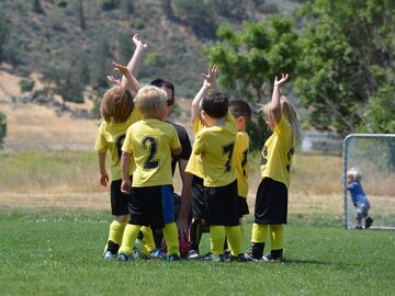 Ein Trainer und sieben Kinder in Fußballtrikots halten die Hände hoch 